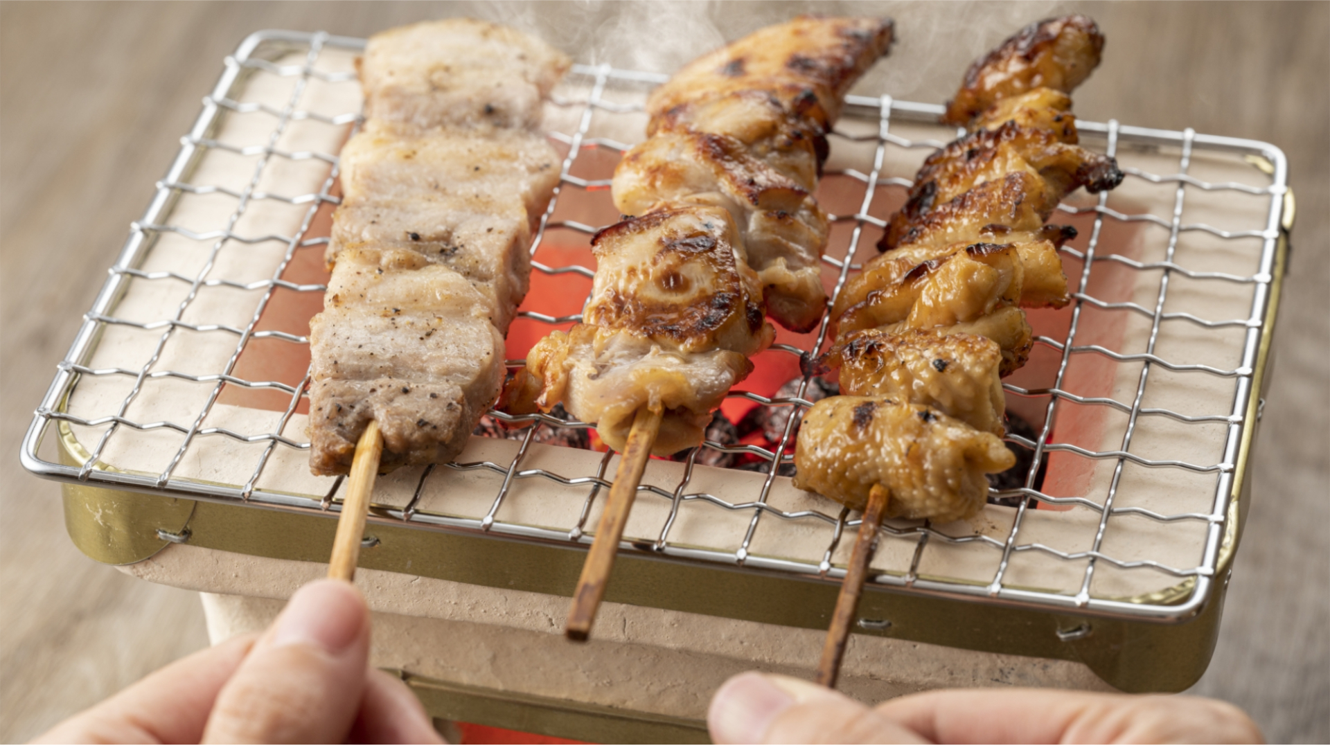 自宅で炭火を起こして網の上で3本の焼き鳥を焼いている画像